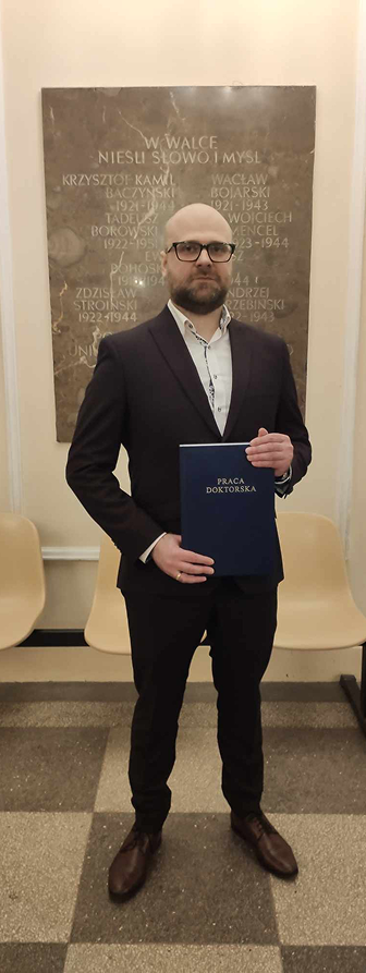I'm standing in a suit after my PhD defense, holding my doctoral dissertation.